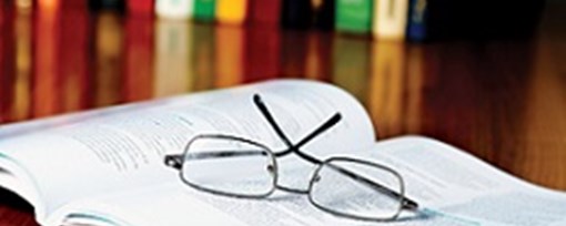 An open reference book with reading glasses resting on top.  